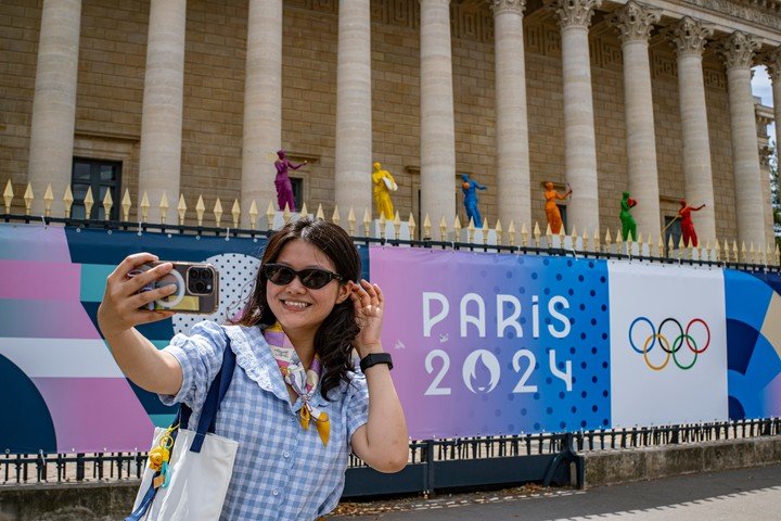 Una turista posando para fotografías con esculturas y decoraciones temáticas de los Juegos Olímpicos frente a la Asamblea Nacional, en París, Francia. 