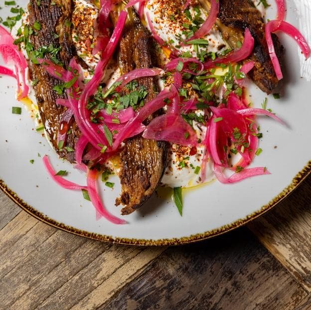La exquisita berenjena rustida con tahini, labhné de hierbas, encurtido de cebolla roja y sésamo del restaurante libanés Aredna. DR